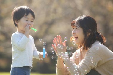 Asyalı anne ve küçük oğlu sabun köpüğü üflüyorlar.
