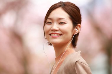 Genç Asyalı kadın kulaklıkla müzik dinliyor.