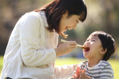 Asyalı anne oğluyla parkta yemek yiyor.