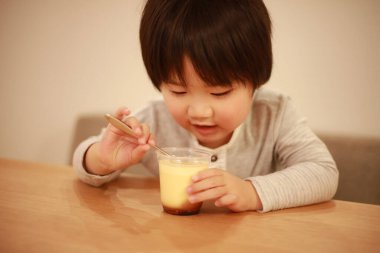 Asyalı küçük çocuk mutfakta puding yiyor.