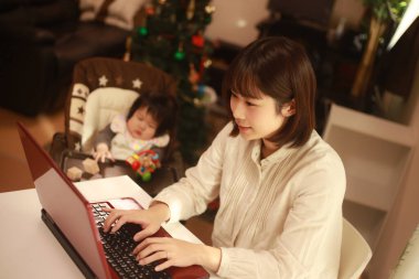 Küçük kızı sandalyede otururken genç anne dizüstü bilgisayar kullanıyor.