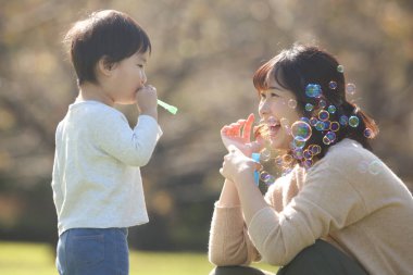 Asyalı anne ve küçük oğlu sabun köpüğü üflüyorlar.
