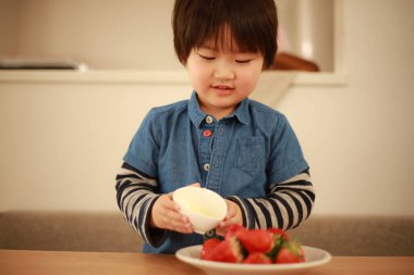 Küçük çocuk mutfakta çilek yiyor.