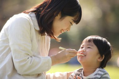 Asyalı anne oğluyla parkta yemek yiyor.