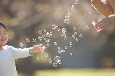 Asyalı anne ve küçük oğlu sabun köpüğü üflüyorlar.