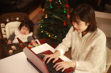 Küçük kızı sandalyede otururken genç anne dizüstü bilgisayar kullanıyor.