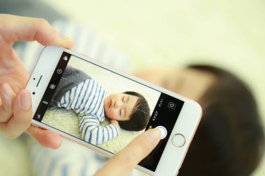 Oğlu yatakta uyurken akıllı telefon kullanan genç bir kadın.