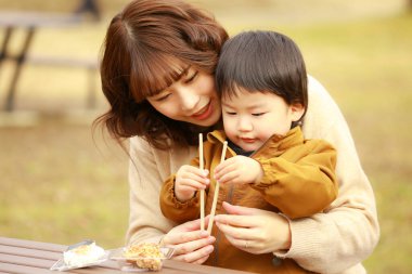 Genç Asyalı anne oğluyla parkta yemek yiyor.  