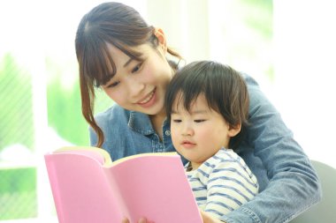 Küçük sevimli oğlu olan genç bir anne evde kitap okuyor.