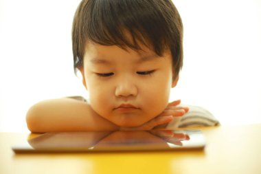 Küçük tatlı Asyalı çocuk oturup tablet bilgisayar kullanıyor.