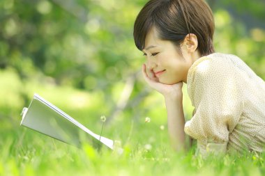 Parkta kitap okuyan Asyalı genç kadının portresi. 