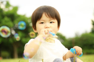 Parkta sabun köpüğü üfleyen Asyalı küçük çocuk. 