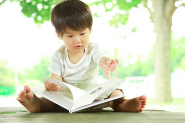 Asyalı küçük çocuk parkta kitap okuyor. 