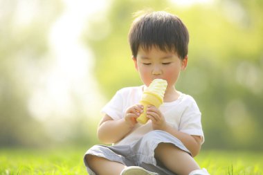 Yeşil çimlerin üzerinde dondurma yiyen tatlı küçük çocuk.