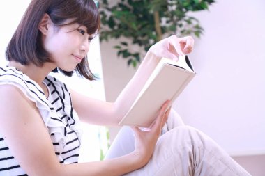 güzel genç Asyalı kadın evde kitap okuyor.