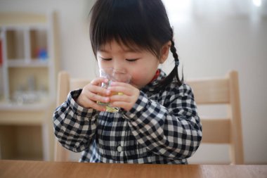 Küçük çocuk evde camdan su içiyor. 