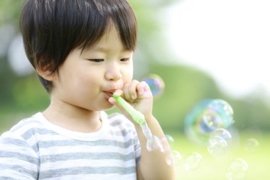 Parkta sabun köpüğü üfleyen Asyalı küçük çocuk. 