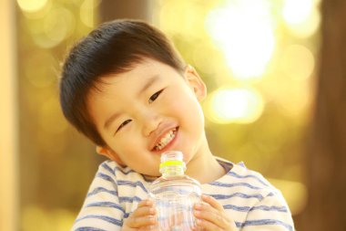 Küçük çocuk şişeden su içiyor. 