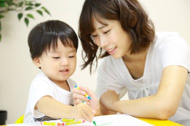 Anne ve oğul beyaz kağıda boya kalemleri çiziyor.