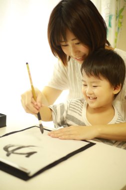 Anne ve oğul fırçayla yazı alıştırması yapıyorlar.