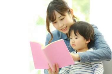 Küçük sevimli oğlu olan genç bir anne evde kitap okuyor.