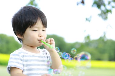 Parkta sabun köpüğü üfleyen Asyalı küçük çocuk. 