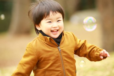 Küçük çocuk parkta sabun köpüğüyle oynuyor.