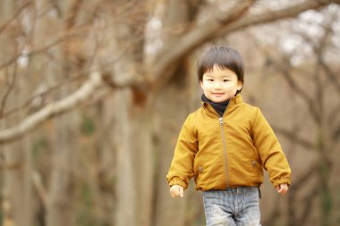Sonbahar parkında yürüyen sarı ceketli şirin bir çocuğun portresi.