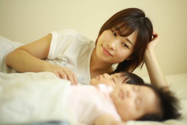 Mutlu Asyalı anne uyuyan oğlana ve kızına bakıyor 