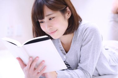 güzel genç Asyalı kadın evde kitap okuyor.