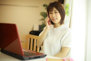 Genç Japon kadın evde çalışırken kırmızı laptop kullanıyor.