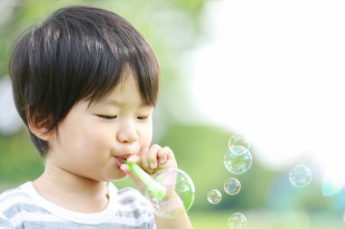 Parkta sabun köpüğü üfleyen Asyalı küçük çocuk. 