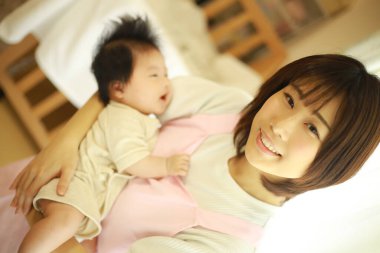 Asyalı genç anne, küçük tatlı kızını kucağında tutuyor. 