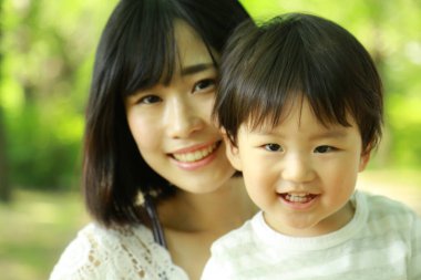 Genç Asyalı anne oğluyla parkta eğleniyor.  