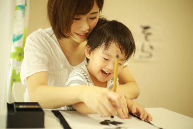 Anne ve oğul fırçayla yazı alıştırması yapıyorlar.