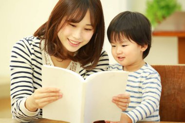 Küçük sevimli oğlu olan genç bir anne evde kitap okuyor.