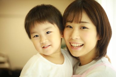 Asyalı genç kadın ve küçük oğlu gülümsüyor. 
