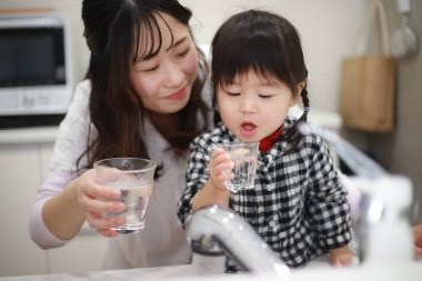 Anne ve kızı musluk suyu içiyor.