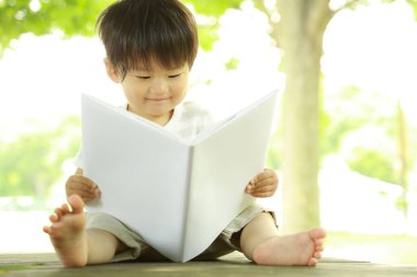 Parkta elinde kitapla yakışıklı Asyalı bir çocuk. 