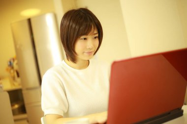 Genç Japon kadın evde çalışırken kırmızı laptop kullanıyor.