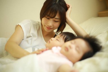Mutlu Asyalı anne uyuyan oğlana ve kızına bakıyor 