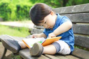 Parkta kitabı olan sevimli Asyalı çocuk. 