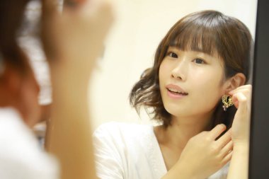Genç Asyalı kadın aynaya makyaj yapıyor.