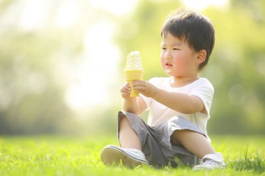 Yeşil çimlerin üzerinde dondurma yiyen tatlı küçük çocuk.