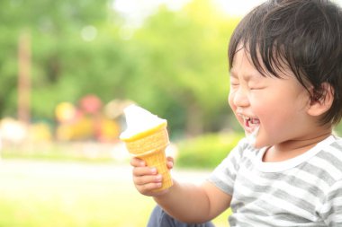 Parkta dondurma yiyen Asyalı küçük çocuk. 