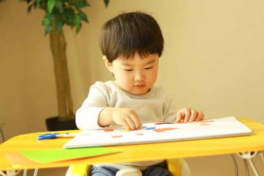 Küçük çocuk evde deftere yazıyor.