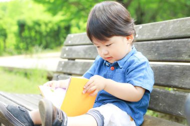 Parkta kitabı olan sevimli Asyalı çocuk. 