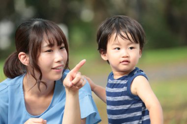 Genç Asyalı anne parkta küçük oğluna bir şey gösteriyor.  