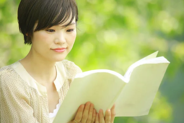 公園で本を読んでいる若いアジア人女性の肖像画 — ストック写真