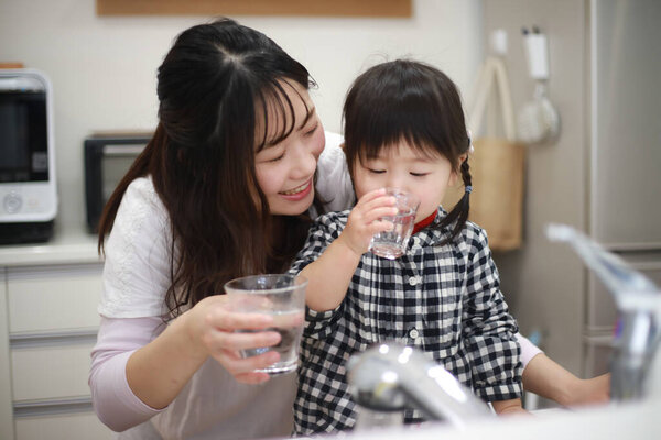 young mother and her daughter drinking water from glasses in kitchen